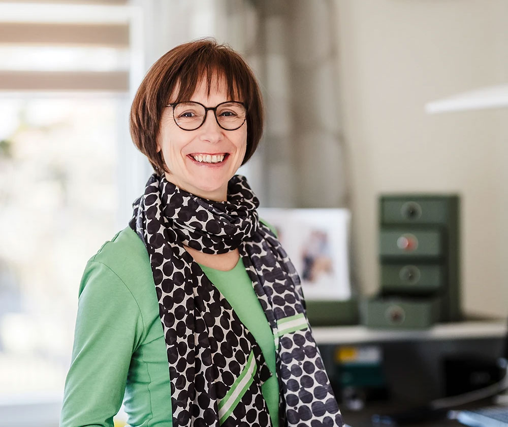 Heike Jurke steht am Schreibtisch mit einem Aktenordner vor sich.